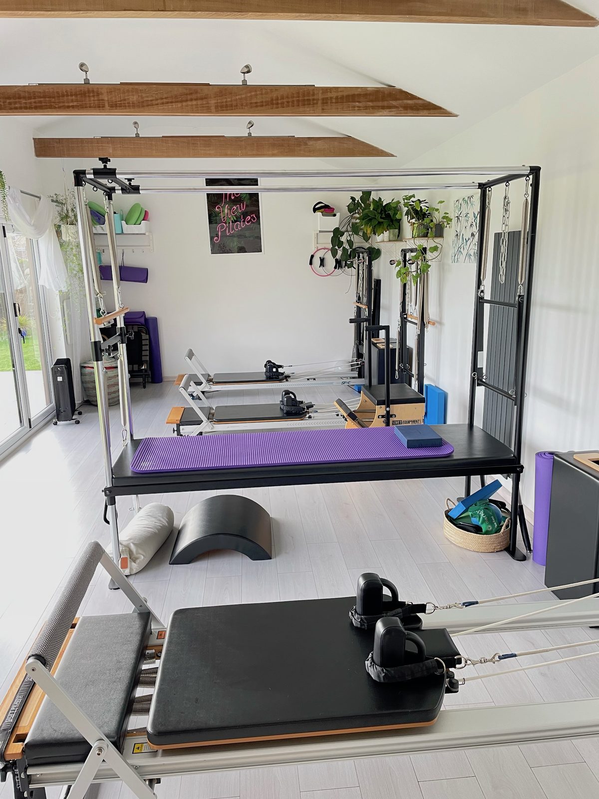 The studio seen along its length: Cadillac, reformer, arc barrel and a vase of flowers, with the doors and garden at the far end.