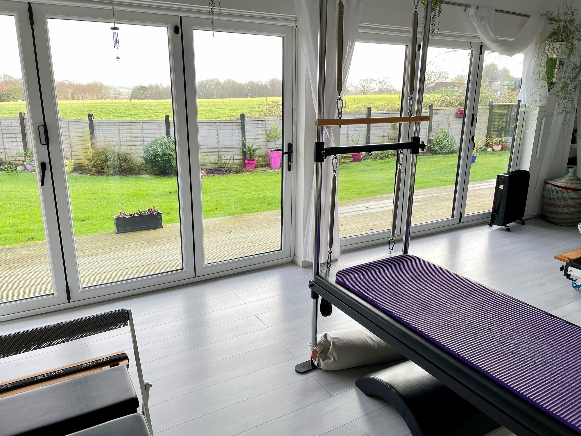 Inside The View Pilates studio at Broad Oak: the bifold doors open onto lawn and a green field, with a reformer in the foreground.